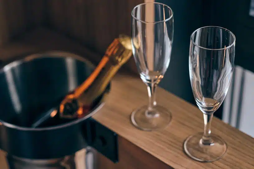 Neben 2 leeren Sektgläsern steht ein Metalleimer, der eine Champagnerflasche enthält.