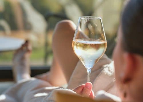 Une femme tient un verre de Champagne rempli dans sa main au restaurant de l'Hôtel LOISIUM Champagne. Alors qu'elle lève le verre élégant, les bulles dorées dansent et scintillent à l'intérieur, reflétant l'atmosphère festive du restaurant.