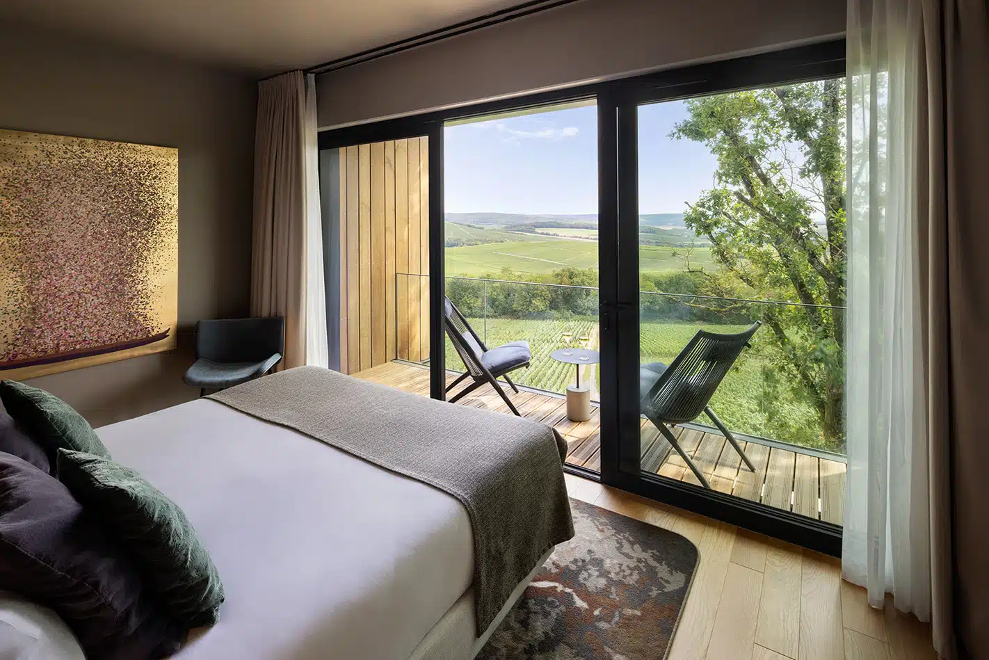 Chambre d’hôtel moderne avec grand lit, balcon et vue sur les vignobles de Champagne.