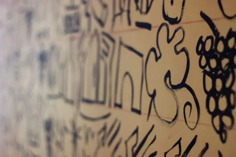 Close-up of a wall drawing featuring stylized LOISIUM motifs, including grapes, architecture, and abstract shapes, in black on a beige background.