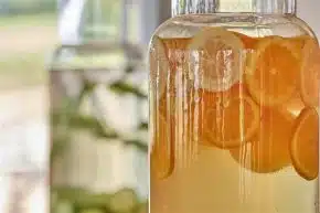 Glass jar filled with water and fresh lemon and orange slices, with another jar of cucumber slices in the background.